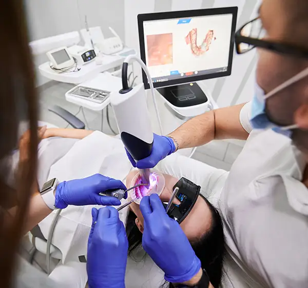 Dental professionals using an intraoral scanner to take precise digital impressions of a patient's teeth, with a monitor showing the scanned results in real-time.